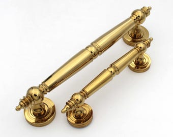 May include: Two gold-colored cabinet handles. One is larger, with a length of approximately 10 inches, and the other is smaller, about 6 inches long. Both have a classic, ornate design with decorative finials and circular base plates.