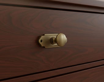 May include: Close-up of a dark brown wooden cabinet with a brass-colored latch. The latch has a rectangular base and a round knob. The wood grain is visible, adding texture to the surface. The cabinet appears to be part of a larger furniture piece.