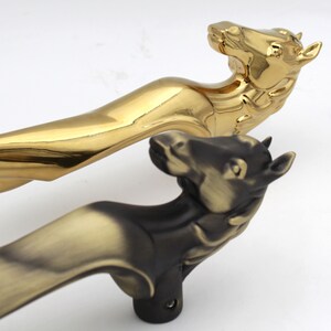 Könnte beinhalten: Zwei Türklinken in Form von Pferden. Eine ist golden und die andere ist schwarz mit einer goldenen Oberfläche.
