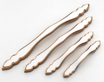 May include: Set of four white and gold cabinet pulls. The pulls have a white center with a gold trim and decorative ends. The pulls are in varying sizes, suitable for different cabinet or drawer dimensions.