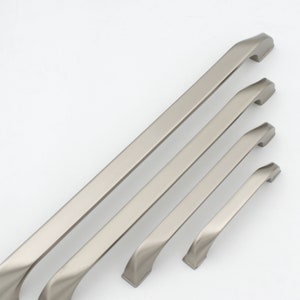 Pode incluir: Quatro puxadores de armário de níquel escovado de diferentes comprimentos. Os puxadores têm uma forma ligeiramente curva e um design moderno.