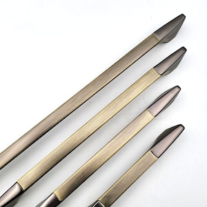 Könnte beinhalten: Vier antike goldfarbene Schranktürgriffe mit gebürsteter Oberfläche. Die Griffe sind diagonal angeordnet, wobei der längste Griff oben und der kürzeste Griff unten ist.