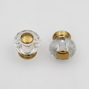 May include: Two clear glass cabinet knobs with gold metal bases. The knobs have a faceted design and a gold metal top.
