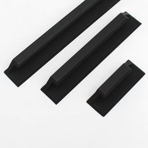 Op de afbeelding: Drie zwarte, rechthoekige kastgrepen met een geribbelde textuur. Elke greep heeft een verhoogde handgreep en een platte basis. De grepen zijn diagonaal geplaatst tegen een witte achtergrond.