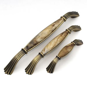 May include: Three antique-style cabinet handles in varying sizes. The handles have a bronze finish with a marbled, cream and brown center section. The handles are arranged diagonally on a white background.