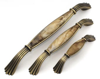 May include: Three antique-style cabinet handles in varying sizes. The handles have a bronze finish with a marbled, cream and brown center section. The handles are arranged diagonally on a white background.