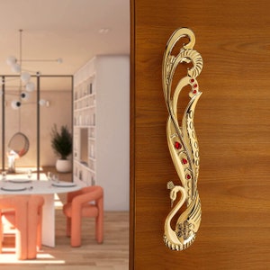 May include: A gold peacock-shaped door handle with red crystal accents. The handle is mounted on a wooden door.
