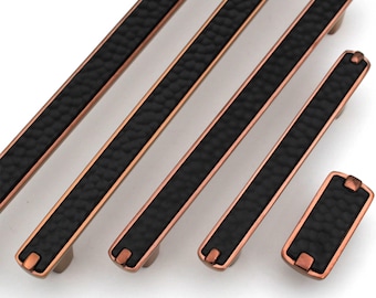 May include: A collection of bronze-colored cabinet pulls with a black textured center. The pulls vary in size, with a rectangular knob at the end of the smallest pull. The hardware has a hammered appearance.