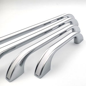 May include: Four chrome cabinet pulls with a white stripe down the centre. The pulls are arranged in a row, with the largest pull on the right and the smallest pull on the left.
