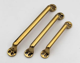 May include: Three gold-colored cabinet pulls of varying sizes. Each pull has a straight bar with rounded ends and three screw holes. The pulls are arranged diagonally against a white background, showcasing their polished finish.