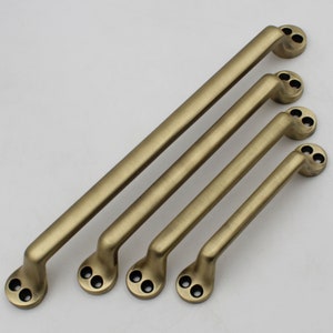 Könnte beinhalten: Vier antike goldfarbene Schrankgriffe mit gebürsteter Oberfläche. Die Griffe sind nach Größe geordnet, der größte oben und der kleinste unten.