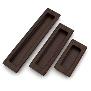 May include: Three brown wooden cabinet door pulls with a rectangular recessed design. The pulls are different sizes.