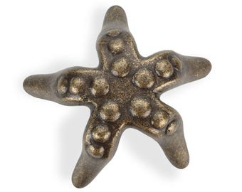 May include: Bronze-colored starfish-shaped decorative knob with a textured surface and raised circular details. The five-pointed star has a vintage, antique appearance. Ideal for coastal or nautical-themed decor.