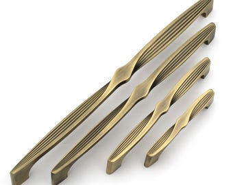 May include: A collection of five antique brass cabinet pulls in varying sizes. Each pull features a ribbed design on the handle and a decorative center. The pulls are arranged diagonally against a white background.