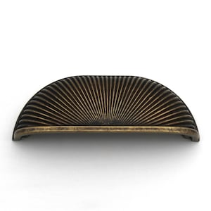 Può includere: Una maniglia per mobili semicircolare con finitura in bronzo scuro e un motivo a raggiera di creste in rilievo. L'accessorio presenta un design curvo a ventaglio con una barra orizzontale liscia sul bordo inferiore per la presa.