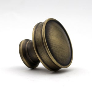 May include: A bronze cabinet knob with a rounded face and a cylindrical base. The knob has a vintage aesthetic, with a slightly distressed finish. The hardware is designed for furniture and home decor.