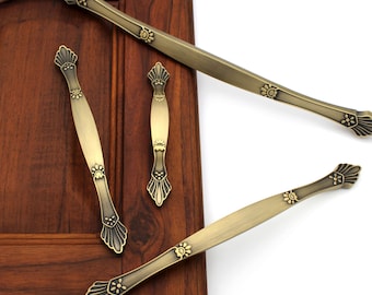May include: Three antique gold cabinet pulls with ornate floral designs. The pulls are shown on a wooden surface.