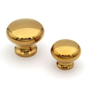 May include: Two gold-coloured cabinet knobs with a shiny, reflective surface. The knobs have a rounded, dome-like top and a short, cylindrical base. One knob is larger than the other. These are ideal for adding a touch of elegance to furniture.