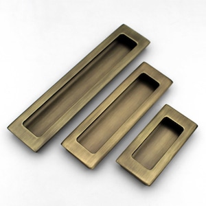 Peut inclure: Trois poignées de tiroir encastrées en laiton antique de différentes tailles. Chaque poignée a une forme rectangulaire avec une zone de prise de doigt encastrée. Les poignées sont disposées en diagonale sur un fond blanc, mettant en valeur leur finition vieillie.