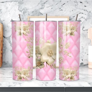 May include: Three pink insulated tumblers with a floral design. The tumblers have a quilted pattern and are decorated with large cream-coloured flowers and gold accents. Each tumbler has a silver lid and a straw.