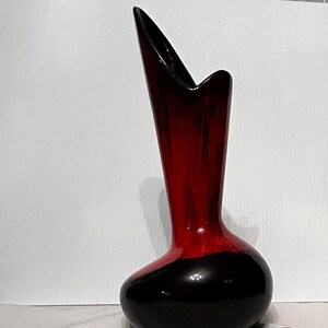 May include: A tall, ceramic vase with a striking design. The vase has a glossy finish with a colour gradient, transitioning from a deep black base to a vibrant red upper section. The top has a unique, asymmetrical shape. A decorative piece for the home.