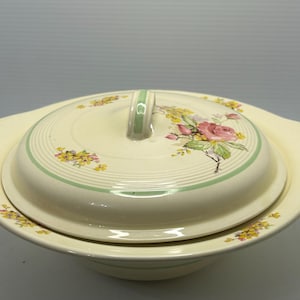 Peut inclure: Plat de service en céramique crème avec couvercle. Le couvercle présente un motif floral avec des roses roses et des fleurs jaunes, des rayures vertes et une poignée. Le plat a des poignées de chaque côté.