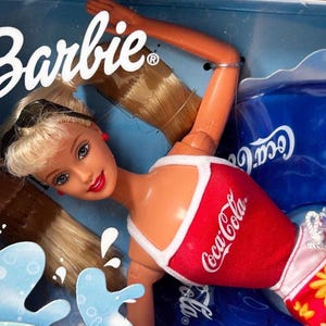 Peut inclure: Une poupée Barbie aux cheveux blonds coiffés en queue de cheval haute, portant un débardeur rouge avec le logo Coca-Cola blanc et des bordures blanches. La poupée a des yeux bleus, du rouge à lèvres et des lunettes de soleil noires sur la tête.