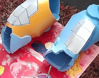May include: Two foam pieces painted blue and yellow with a white geometric pattern. The pieces are on a red and white paint palette with paint brushes and a jar of paint.