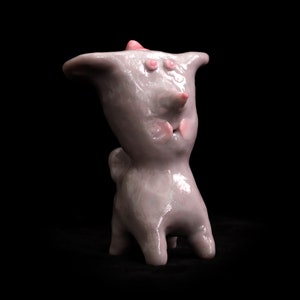 Peut inclure: Une petite sculpture en céramique peinte à la main représentant une créature au long museau, aux grands yeux et à la langue rose qui sort. La sculpture est de couleur violet clair et a une finition brillante.