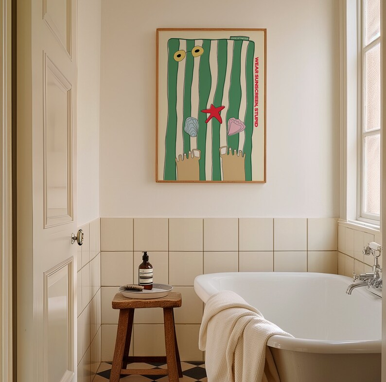 May include: A white bathtub with a white towel draped over the edge. A wooden stool with a bottle of soap and a brush sits next to the tub. A framed poster with green and white stripes and the text "WEAR SUNSCREEN, STUPID" hangs on the wall above the tub.