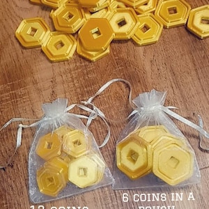 May include: Two organza bags filled with gold-colored coins. The bag on the left contains 12 coins that are 1 inch in size. The bag on the right contains 6 coins that are 1.5 inches in size. The text "12 coins 1" size" is below the left bag and the text "6 coins in a pouch 1.5" coins" is below the right bag.