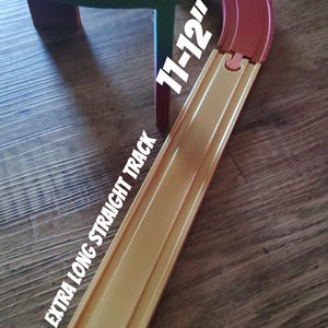 Peut inclure: Un ensemble de circuits de train jouet en bois avec une section incurvée surélevée et une longue voie droite. La voie droite est étiquetée "EXTRA LONG STRAIGHT TRACK" et mesure 28-30 cm de long. L'ensemble est peint en plusieurs couleurs.