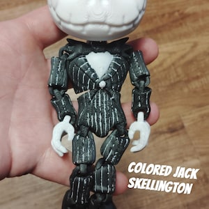 May include: A 3D printed articulated figure of Jack Skellington from the Nightmare Before Christmas movie. The figure is painted in black and white with a pinstripe suit and a bow tie. The figure is holding its hands up in a gesture of surprise. The text "COLORED JACK SKELLINGTON" is printed below the figure.