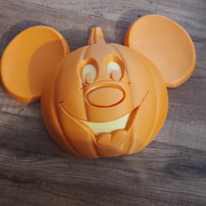 Puede incluir: Decoración con forma de calabaza naranja con orejas grandes y redondas y una cara sonriente. La calabaza tiene boca y ojos de color amarillo claro. Una divertida decoración temática de Halloween o otoño.