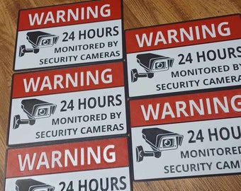 May include: Five red and white warning signs with black text and a black and white image of a security camera. The signs read "WARNING 24 HOURS MONITORED BY SECURITY CAMERAS".