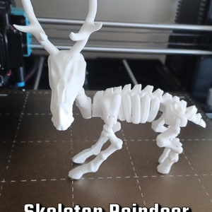 以下が含まれることがあります： 白いプラスチック製の骨格のトナカイの置物。トナカイは、グリッドパターンが施された茶色の表面に立っています。