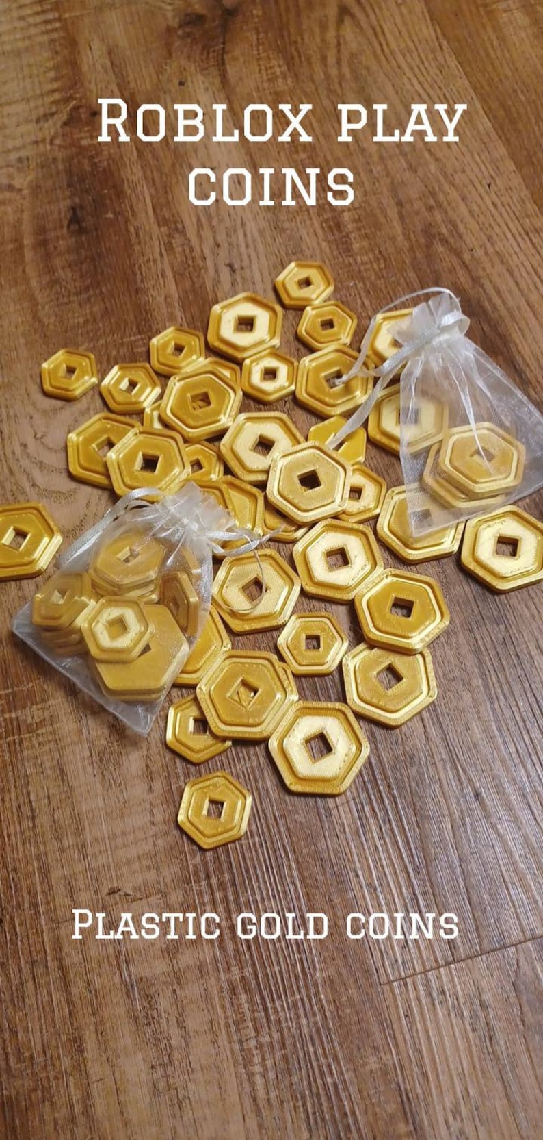May include: A pile of gold plastic Roblox play coins in a white mesh bag. The coins are shaped like octagons with a square hole in the center. The text "ROBLOX PLAY COINS" and "PLASTIC GOLD COINS" is visible in the image.