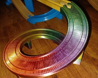 Può includere: Un pezzo di pista in plastica arcobaleno per un set di auto da corsa giocattolo. La pista è curva e ha un bordo rialzato. La pista è sostenuta da tre gambe.