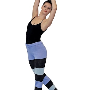 May include: A woman wearing a black tank top and blue and black striped knit leggings. She is standing on her toes with her arms raised above her head.