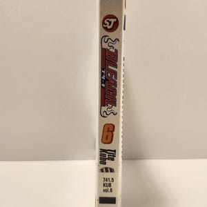 Puede incluir: Un volumen de manga blanco con el t&iacute;tulo "Bleach" en letras rojas y negras. El n&uacute;mero "6" es visible, junto con "Title Kubo" y texto japon&eacute;s. El volumen tiene un dise&ntilde;o estilizado, con el logo SJ en la parte superior.