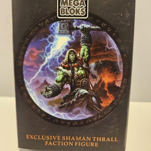 May include: A Mega Bloks box featuring an illustration of a green-skinned Shaman Thrall figure wielding a hammer, with lightning and fire in the background. The box is black with the text "EXCLUSIVE SHAMAN THRALL FACTION FIGURE".
