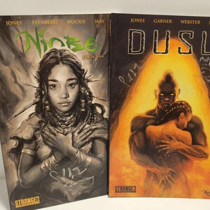 May include: Two comic book covers. The left cover features a woman with intricate jewelry and the title "Ninbe". The right cover shows a muscular figure embracing another, with the title "Dusu". Both are from Stranger Comics.