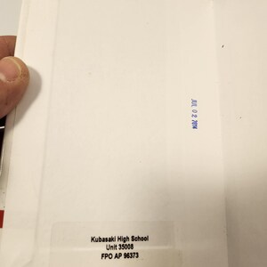Puede incluir: Sobre blanco abierto con borde rojo y azul. El interior est&aacute; en blanco, con un sello azul que dice "JUL 02 2014". Una etiqueta muestra "Kubasaki High School, Unit 35008, FPO AP 96373."
