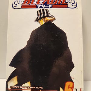Puede incluir: Una novela gr&aacute;fica blanca titulada "Bleach" con un logotipo estilizado y texto japon&eacute;s. La portada presenta un personaje con abrigo y sombrero negros. El n&uacute;mero de volumen 6 est&aacute; en un recuadro rojo y naranja. El autor es Tite Kubo.