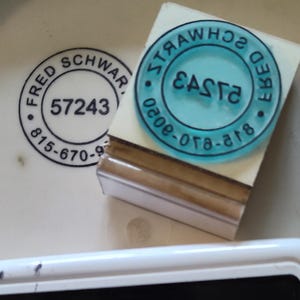 Puede incluir: Una almohadilla de tinta blanca con texto negro que dice "Archival Ink" y "Jet Black". Un sello azul con el texto "Easte" y "Fred Schwar" está al lado de la almohadilla de tinta. También es visible un sello con el texto "Fred Schwar" y el número "57243".