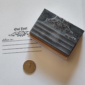 May include: A rectangular rubber stamp featuring an owl graphic and the text Owl Post and deliver to with four horizontal lines. The stamp is positioned next to a United States quarter coin for scale, showing a stamped impression on paper.
