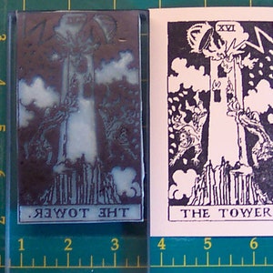 May include: A black and white illustration of the Tower card from a tarot deck. The card shows a tower being struck by lightning, with two figures falling from the top. The text "XVI" and "THE TOWER." are printed on the card.