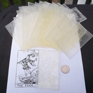 May include: A set of clear plastic tarot card stamps with the Fool card printed on a white sheet of paper. The Fool card shows a man walking on a cliff with a staff and a backpack. The text "THE FOOL" is printed below the image.