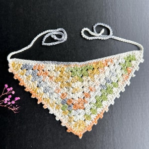 May include: A crocheted triangle scarf in shades of white, green, orange, and gray. The scarf has a fringe border and is tied with a long string.