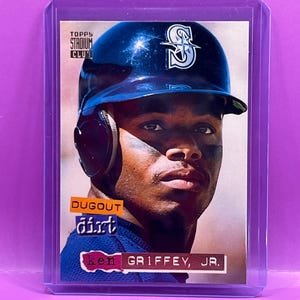 May include: A Ken Griffey Jr. baseball card from the Topps Stadium Club series. The card features a portrait of Griffey in his Seattle Mariners uniform and helmet. The card is encased in a protective plastic sleeve.